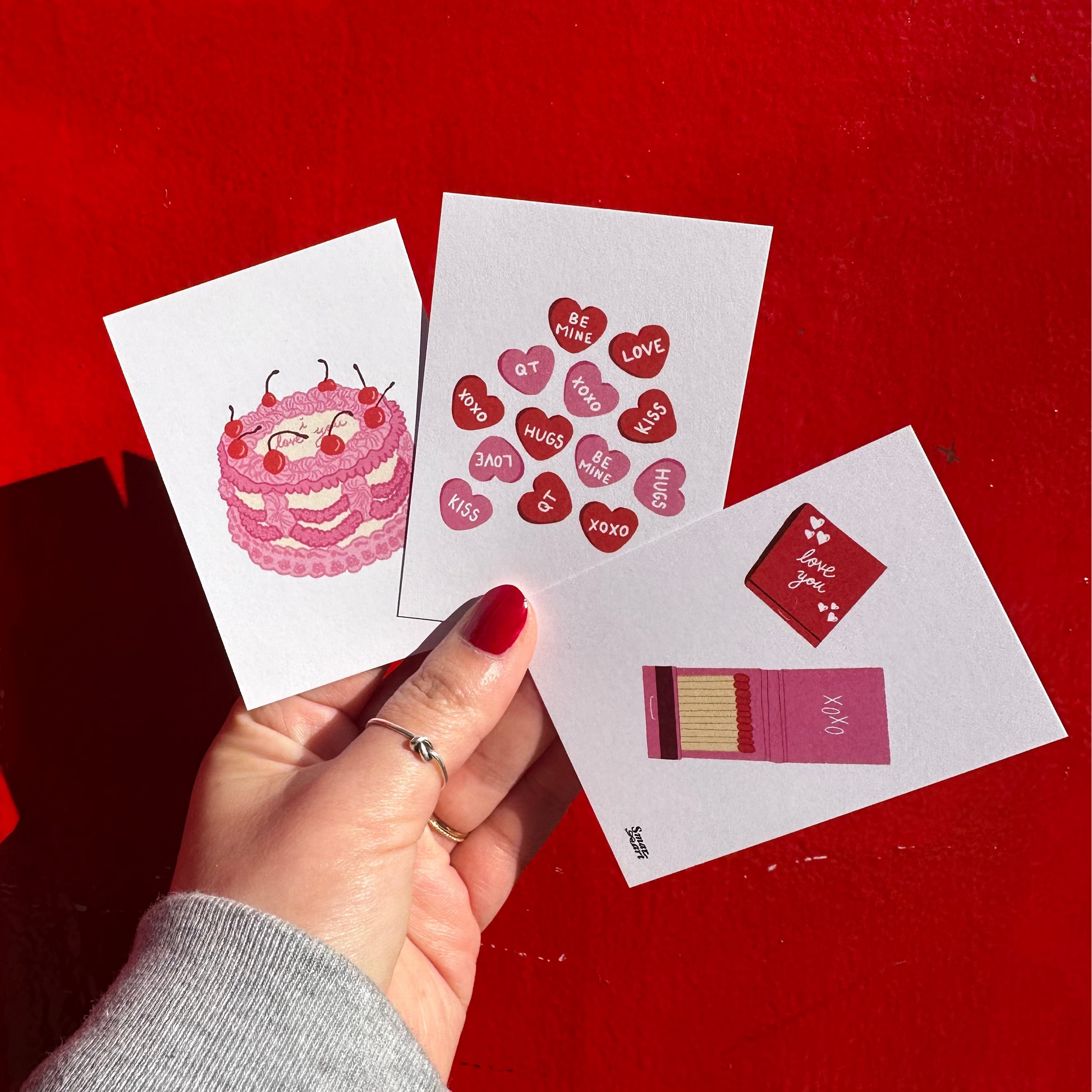 Hand holding a card with a pink character design on a red background